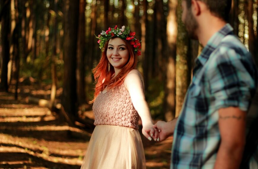 couple holding hands while standing near tree barks